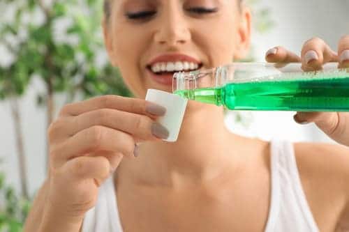 woman holding a bottle of green mouthwash as she pours it into the bottle cap