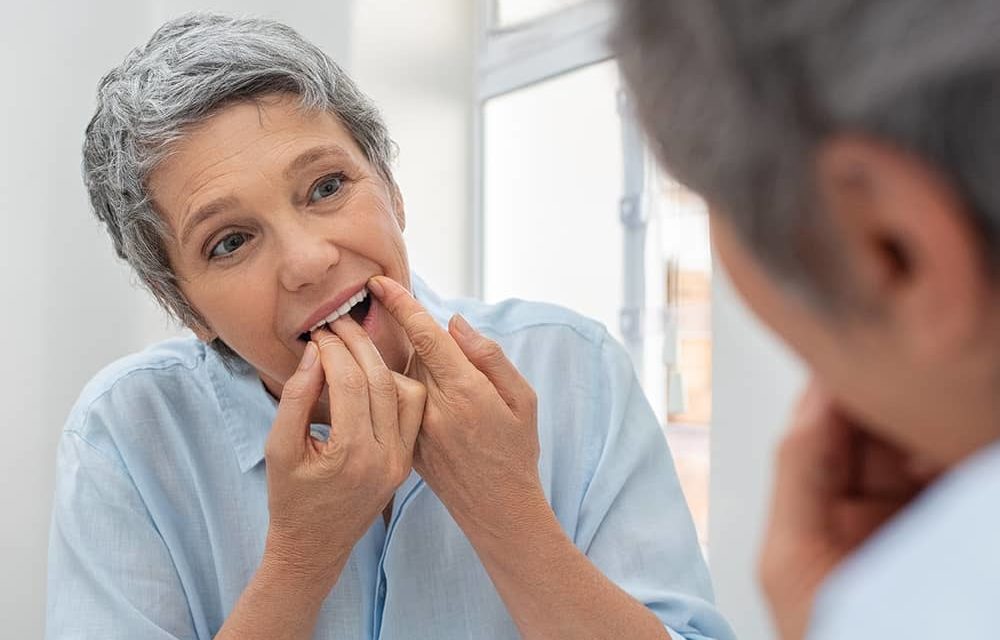 Woman caring for her denture implants by flossing