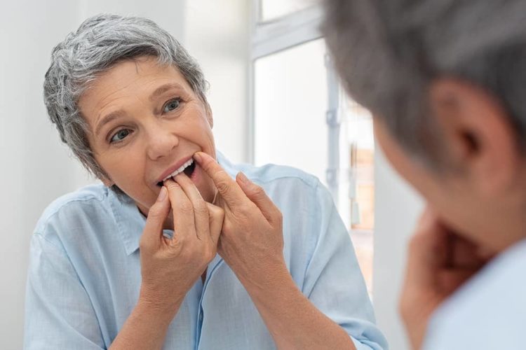 Woman caring for her denture implants by flossing